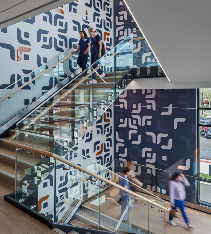 Open glass staircase with a bold geometric wall pattern, students and staff moving between floors.