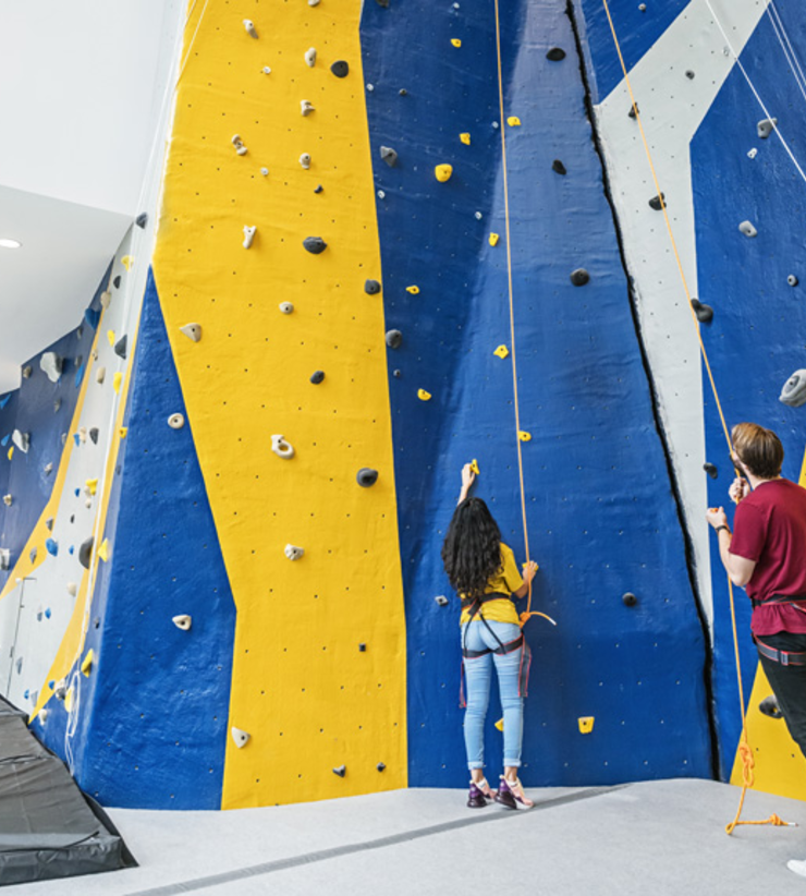 Two students stand at the bottom of the rock-climbing wall