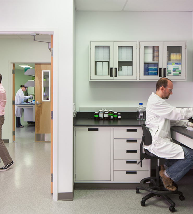 One man enters the lab, another is sitting down and using test tubes