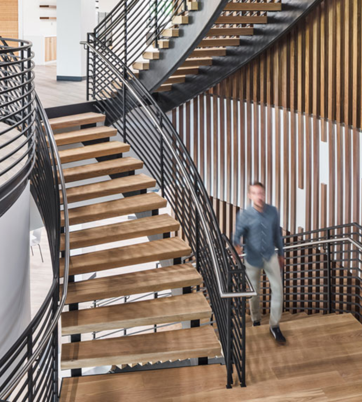 An employee advances from one floor to the next using a staircase with wooden accents