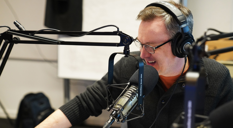 Podcast Host Brian Trainer talks into a microphone
