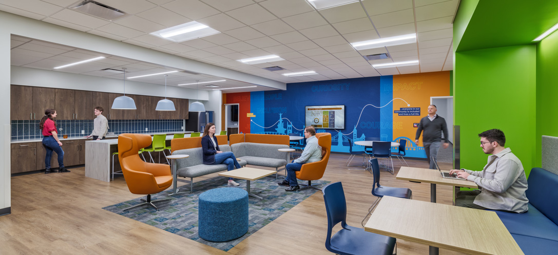 Colorful lounge and workspace at Easterseals Redwood's Cincinnati campus with orange and blue accent walls, a kitchenette, and mixed seating including standing-height desks and a sectional sofa