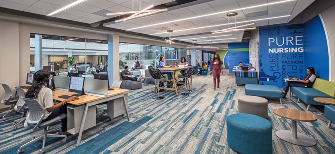 Nursing students studying and collaborating in Galen College of Nursing's open lounge space, with computer workstations, group seating, and a bold blue "Pure Nursing" graphic wall.