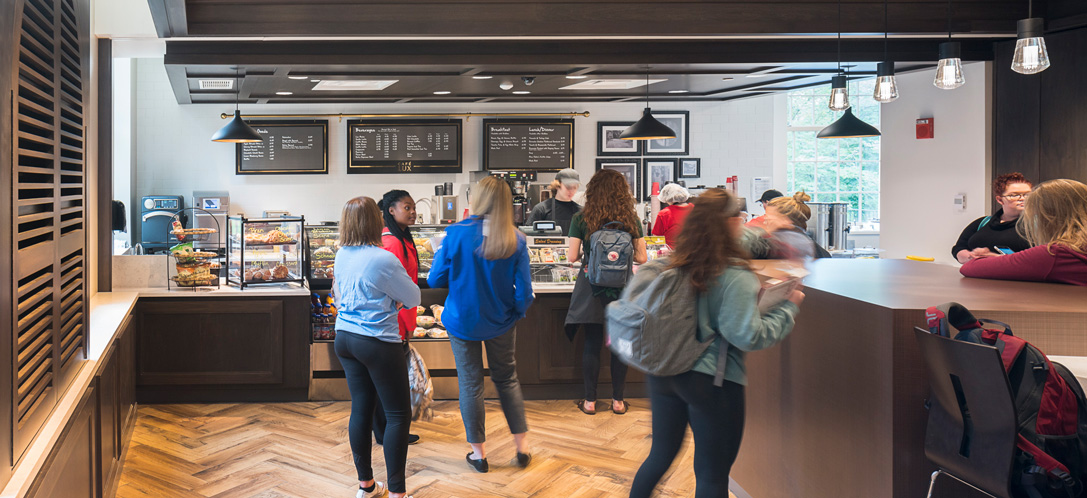 Students lined up at a campus café with menu boards, pastry display cases, and warm wood finishes at Miami University's Armstrong Student Center.
