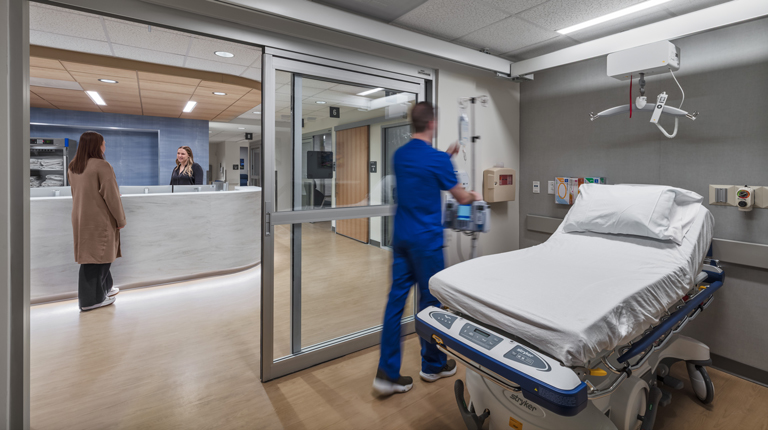 Nurse in room and people talking at desk