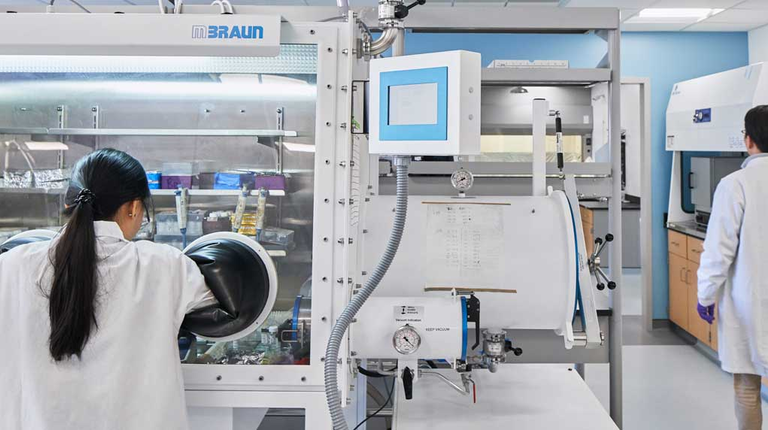 Inside the lab, a student works with her hands inside a large piece of lab equipment